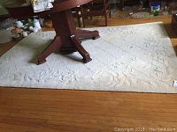 Full view of the beige carpet with a table on top, showing the carpet's size and pattern.