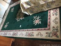 Full view of green wool carpet with floral motif and border, showing condition and size relative to nearby furniture.