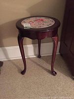 Full view of the small round wooden table with curved legs and floral ceramic insert on top