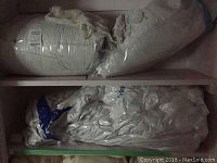 Queen duvet and mattress cover packed in transparent plastic bags on a shelf.