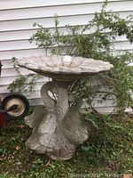 Front view of the concrete birdbath showing the swan figures at the base and the scalloped edge bowl on top.