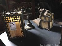 Overview of both antique hanging pendant light fixtures on black cloth, showing metal frames and amber slag glass panels