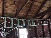Aluminum extension ladder hung on the wooden wall of a shed or garage, showing the ladder fully extended with a rope and pulley system visible.