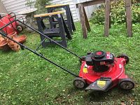 Side view of red Yard Machine lawn mower on grass with black handle and wheels, showing overall condition and grass discharge chute.