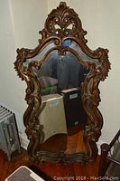 Ornate wooden framed mirror with decorative scrollwork and brown finish, measuring approximately 28 by 55 inches.