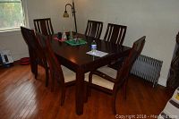 Dining room table with six matching chairs around it, arranged in a room with hardwood floor and windows.