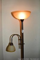 Floor lamp with a tall dark metal stand, an amber upward-facing bowl glass shade on top, and a lower smaller cream-colored curved glass shade on an attached arm, operating with visible pull chains.