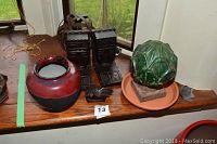 Wooden African style bookends, wood head sculpture, red and black vase, green ceramic art piece on terra cotta saucer, small wooden animal figurine on windowsill.