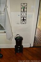 Photo of black antique ornamental heater on hardwood floor beside a white wall and window curtain