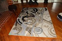 Area rug flat on hardwood floor showing abstract swirl and geometric pattern in shades of gray, black, and beige.