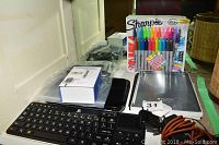Overview of the lot showing boxed iPad Pro cases, Logitech keyboard, remote, voice recorder, Sharpie markers and some cables.