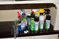 Photo showing various cleaning sprays and aerosol cans on a shelf including Glass Plus, Raid, Lysol, Armor All Tire Foam, and Rust-Oleum products