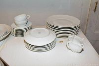 Full set of white Richard Ginori china including stacked plates, saucers, and two cups shown on white surface