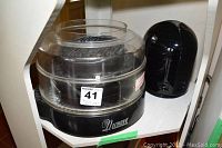 NuWave infrared oven with clear dome lid and black base, placed on white shelf next to black and white appliance (AirFree air purifier)