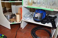 Shelved area showing Bissell Zing vacuum cleaner with multiple attachments and a white electric hair curler set with multiple ceramic curling barrels.