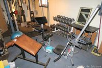 Overview of the exercise equipment including benches, dumbbell rack, rowing machine, exercise balls, and mirror in basement gym setting.