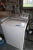 Front view of white Maytag top-loading washing machine in basement setting.
