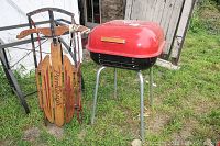 Photo of Parkleigh wooden sled with metal runners and a red charcoal grill with domed lid and four legs on grass outside a shed.