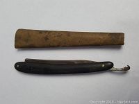 Straight razor with black handle opened beside worn paper/sheath cover.