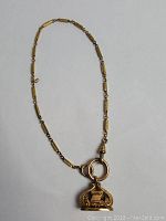 Full view of antique gold-tone pocket watch chain with attached decorative fob charm on white background.