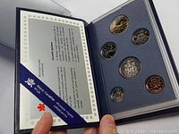 Open presentation box showing six Canadian coins and official certificate inside held in place by blue ribbon.