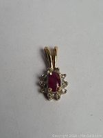 Front close-up photo of a petite gold pendant featuring an oval ruby and surrounded by small diamonds, showing detailed stones and bail.