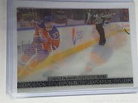 Front view of the Connor McDavid 2017-18 Triple Exposure special insert hockey card encased in a clear protective sleeve showing the triple exposure visual effect and player in Edmonton Oilers uniform on ice with Upper Deck logo.