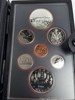View of the seven coins in the black leather-style holding case showing designs including polar bear, caribou, coat of arms, and maple leaf