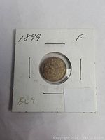 Front view of the 1899 Canadian silver five cent coin enclosed in a white cardboard 2x2 coin holder with handwritten notes '1899' and 'F'. Coin shows circulated condition and patina.