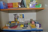 Shelf with multiple office supplies including envelopes, tape, Post-it notes, scissors, and small items.