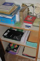 Assorted office supplies on shelves including file folders, notebooks, decorative boxes, green binder clips, and plastic sleeves.