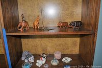 Shelf with wooden animal figurines on top and smaller figurines and decorative items on lower shelf.
