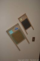 Two vintage water boards mounted on wall with wooden frames and ribbed scrubbing surfaces, one larger with metal ribs and one smaller with black ribs.