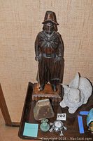 Carved wooden figure, white rabbit sculpture, small bell and trinket on edge of table