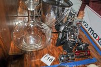 Photo showing glass decanter, metal ice bucket, several metallic bottle openers and bar tools spread on wooden surface.