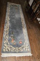Full view of the blue entry rug with floral border on wooden floor.