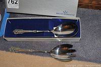Two Wallace Silversmiths serving utensils, spoon and pierced fork, displayed in blue velvet-lined branded boxes.