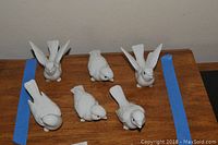 Six white ceramic bird figurines placed on a wooden surface, showing various positions and detail of the birds.