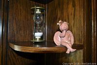 Glass hourglass timer and ceramic cherub angel figurine on wooden shelf.