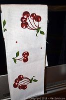 Photo of white waffle weave dish towel featuring a red cherry pattern with green leaves