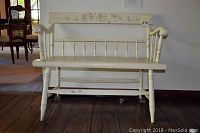 Front view of the cream white vintage bench with spindle legs and floral painted backrest.
