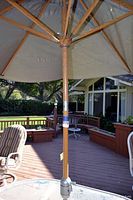 Photo showing full patio umbrella set up on wooden deck with metal base stand and wooden hub and ribs supporting fabric canopy.
