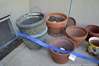 Photo showing multiple garden pots grouped including clay pots and a large textured grey pot.