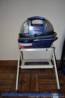 Bissell Spot Bot carpet cleaner sitting on top of Rubbermaid step stool on wooden floor.