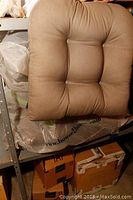 Brown tufted cushion top side shown resting on plastic bag and boxes.