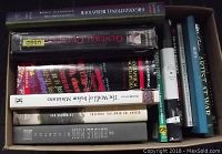 Top down view of 13 assorted books lying flat inside a box. Titles visible include 'Organizational Behaviour', 'General Chemistry', 'Artist at Work', and others. Shows a mix of hardcover and paperback books.