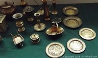 Overhead view of assorted brassware on green cloth including vases, candle sticks, teapot, small ashtray, lidded container, plates and trays.