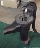 Front and top view of vintage hand water pump showing spout and handle in upright position, black cast iron, used condition.