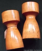 Two solid wood candlesticks in natural wood tones with visible wear and craftsman marks, photographed side by side on a dark green background.