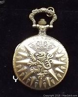 Front cover of the bronze pocket watch with raised dragon design and starburst pattern.